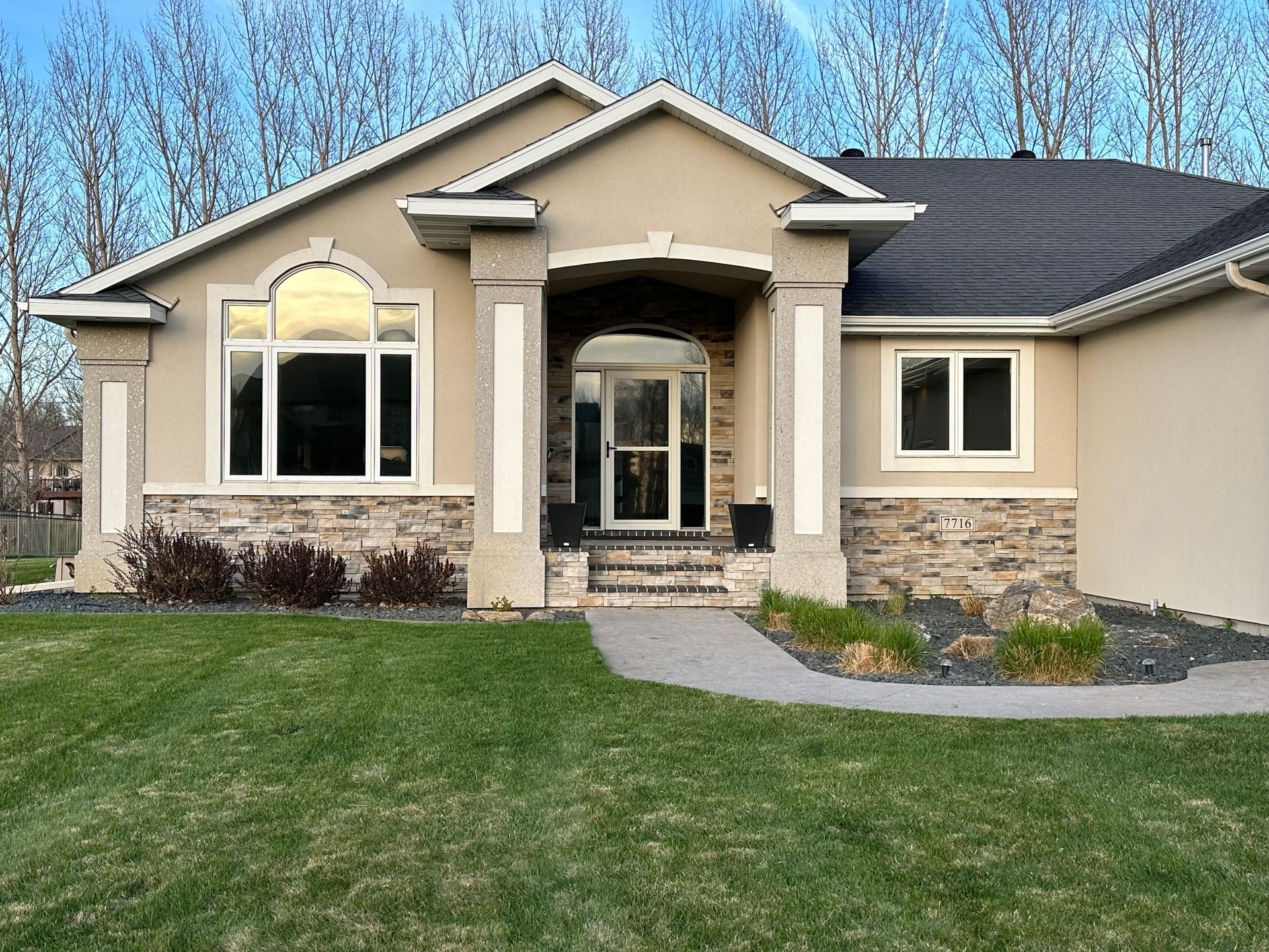 Modern beige house with large arched window, stone accents, and front lawn.